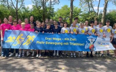 Mehrere Kinder und Jugendliche stehen hinter einem Banner mit dem Slogan: "Drei Wege, ein Ziel! Mehr Bewegung mit Triathlon!"
